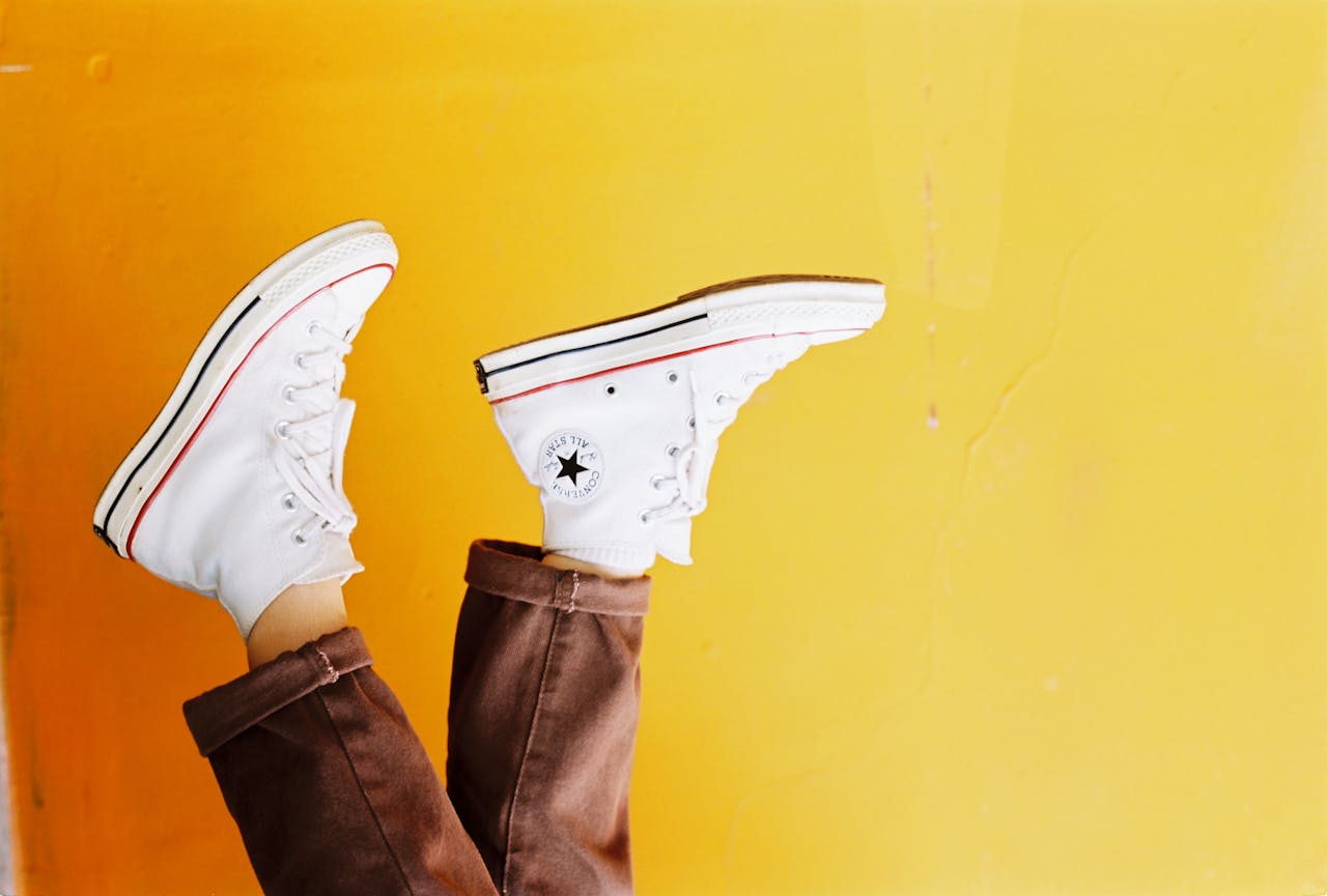 Upside down image of white sneakers against a vibrant yellow background, showcasing trendy footwear style.